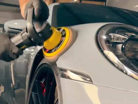 Politriz trabalhando na pintura de um Porsche 911 cinza